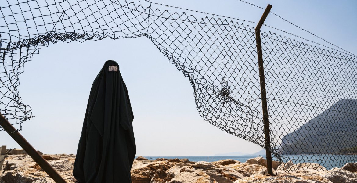 Refugee woman in burka standing behind a fence