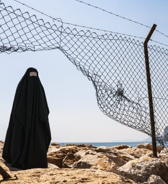 Refugee woman in burka standing behind a fence