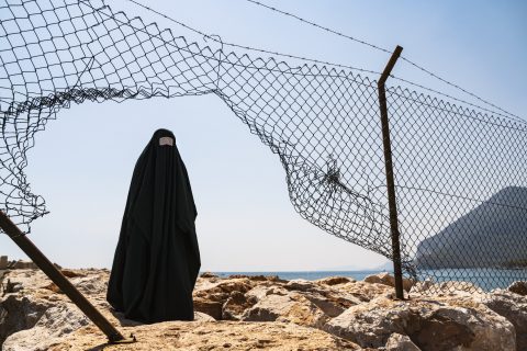 Refugee woman in burka standing behind a fence